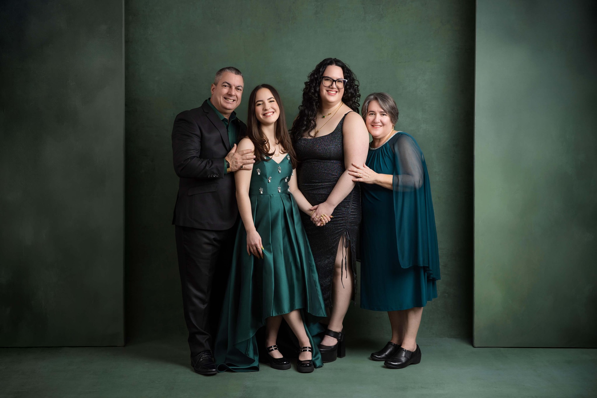 A happy mom and dad stand smiling with their happy teenage daughters in a studio