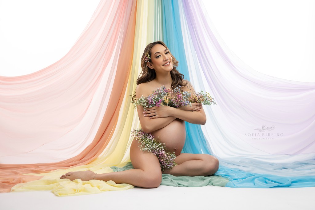 nj maternity photographer captures a mom to be with symbolism of a rainbow baby, draped rainbow fabric and flowers