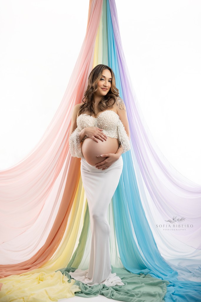 rainbow baby maternity photography- mom in white against a draped rainbow backdrop