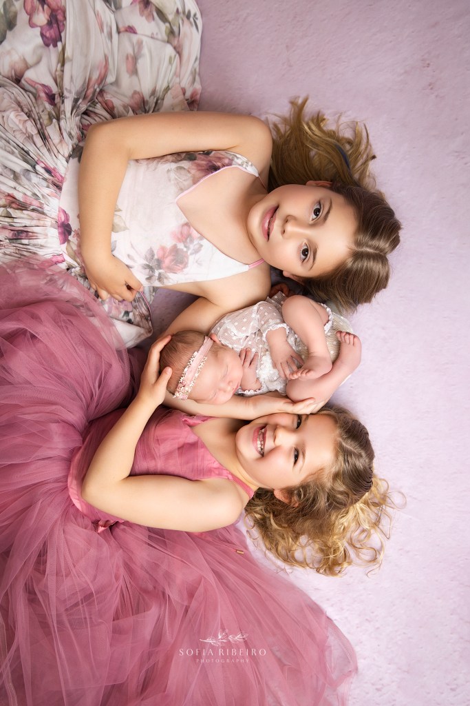 big sisters cradle their newborn sister during photos in an nj newborn photographer's studio