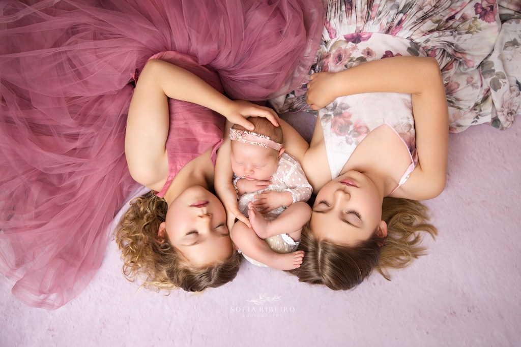 big sisters cradle their newborn sister during photos in an nj newborn photographer's studio