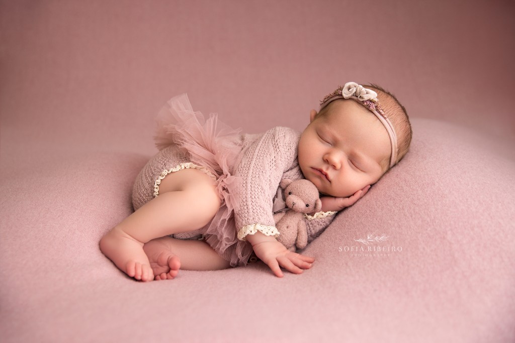 baby girl cradles a pink stuffed bear during her newborn photo session