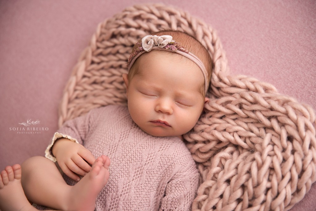 newborn baby girl is framed in a knitted heart in shades of pink