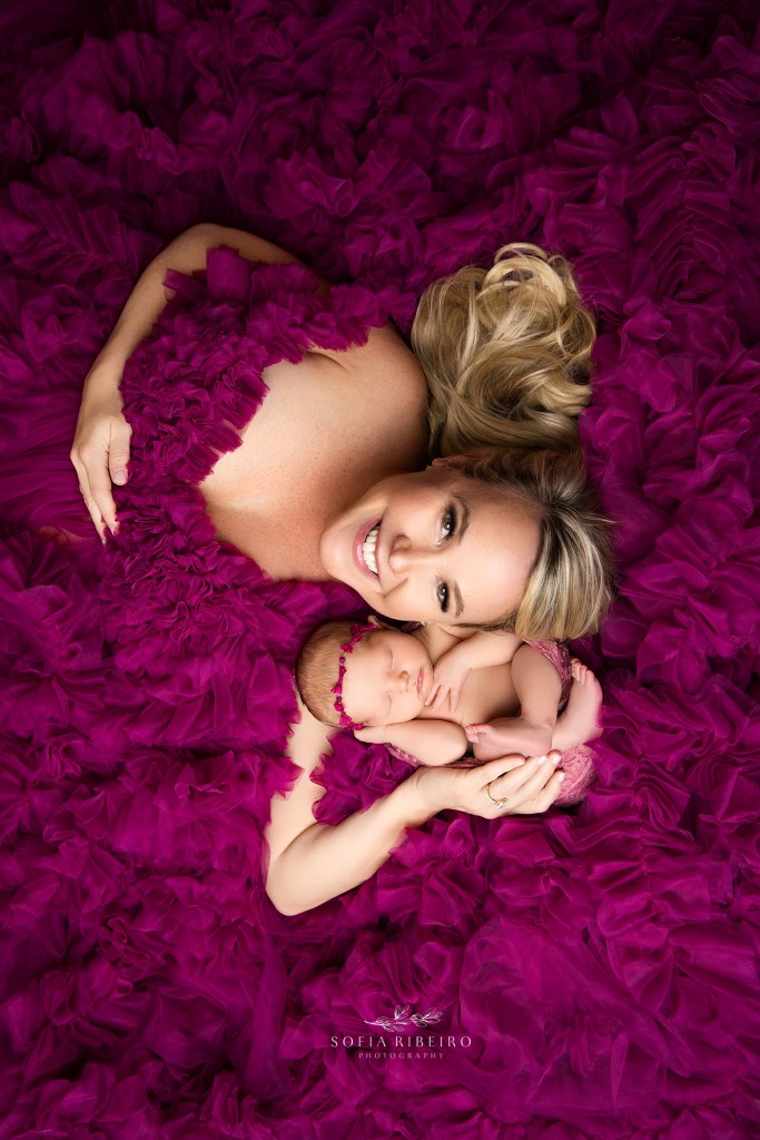 mom and baby lie together in a pink ruffled tulle gown