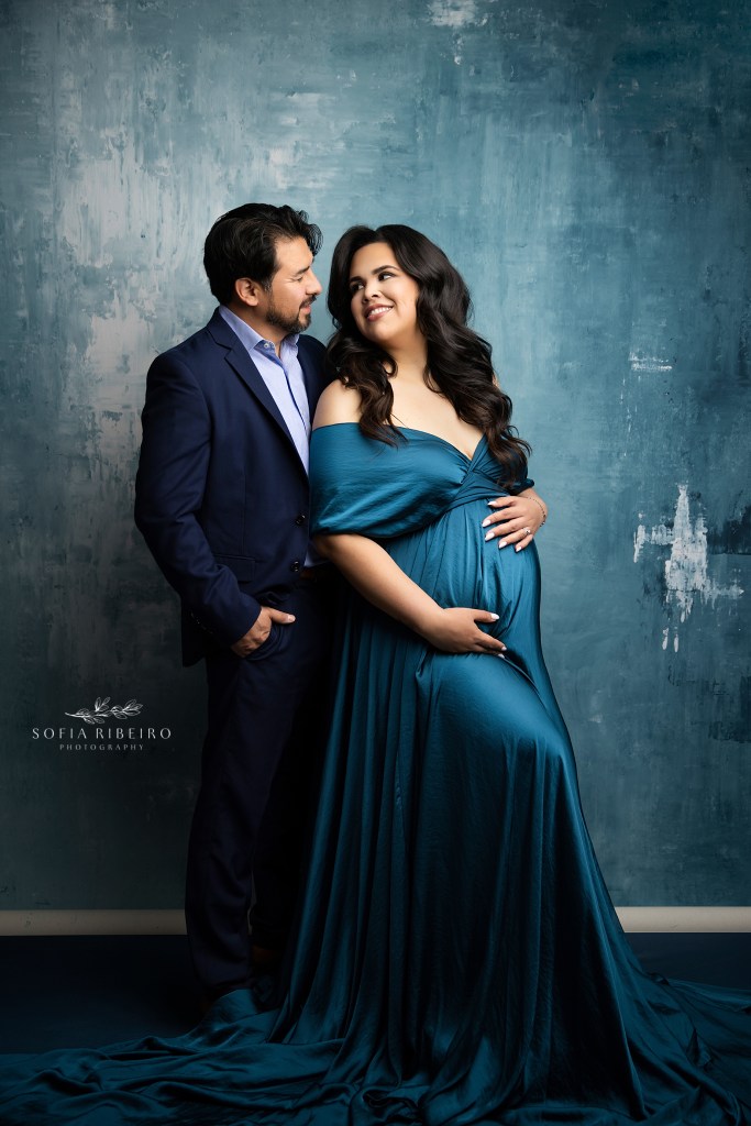 mom and dad to be smile at wach other , in stunning blue looks against a painted backdrop