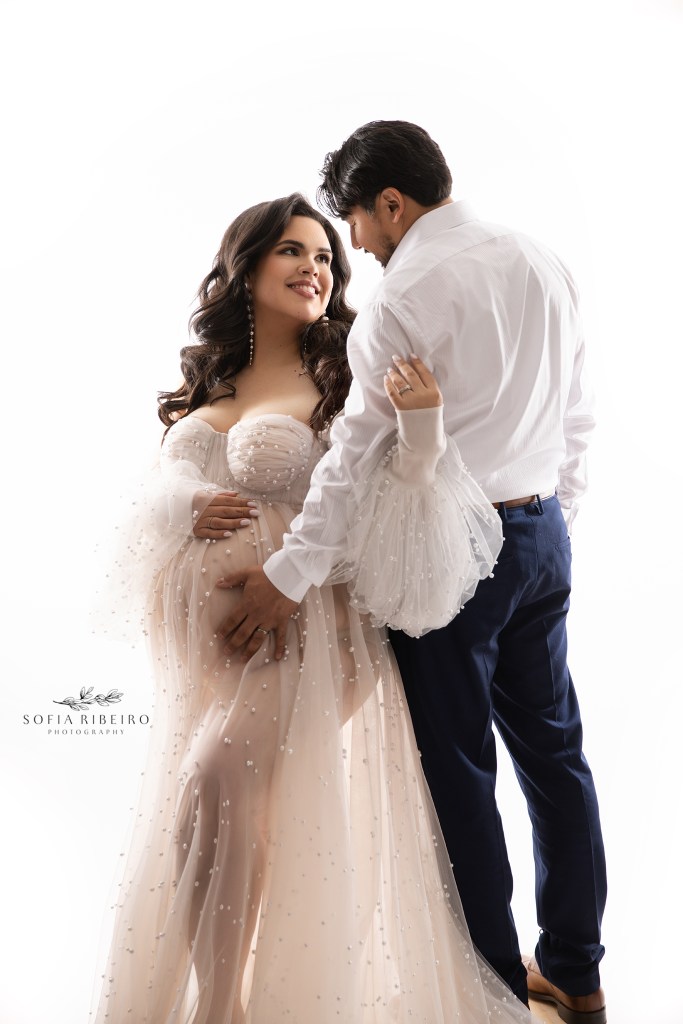 mom and dad to be cradle the baby bump against a highlighted white backdrop