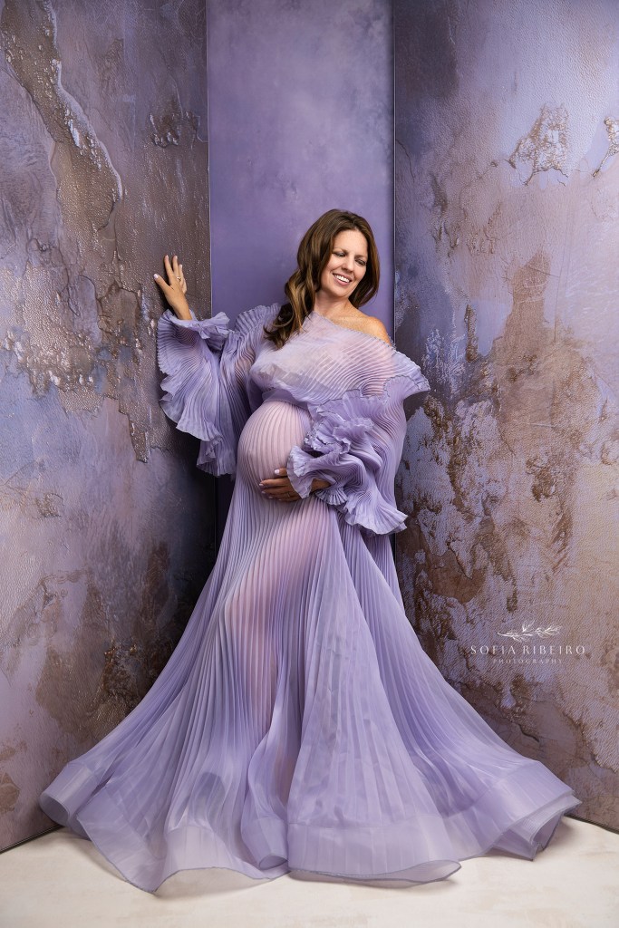 a purple pleated gown highlights moms baby bump against a purple backdrop for maternity photos in nj