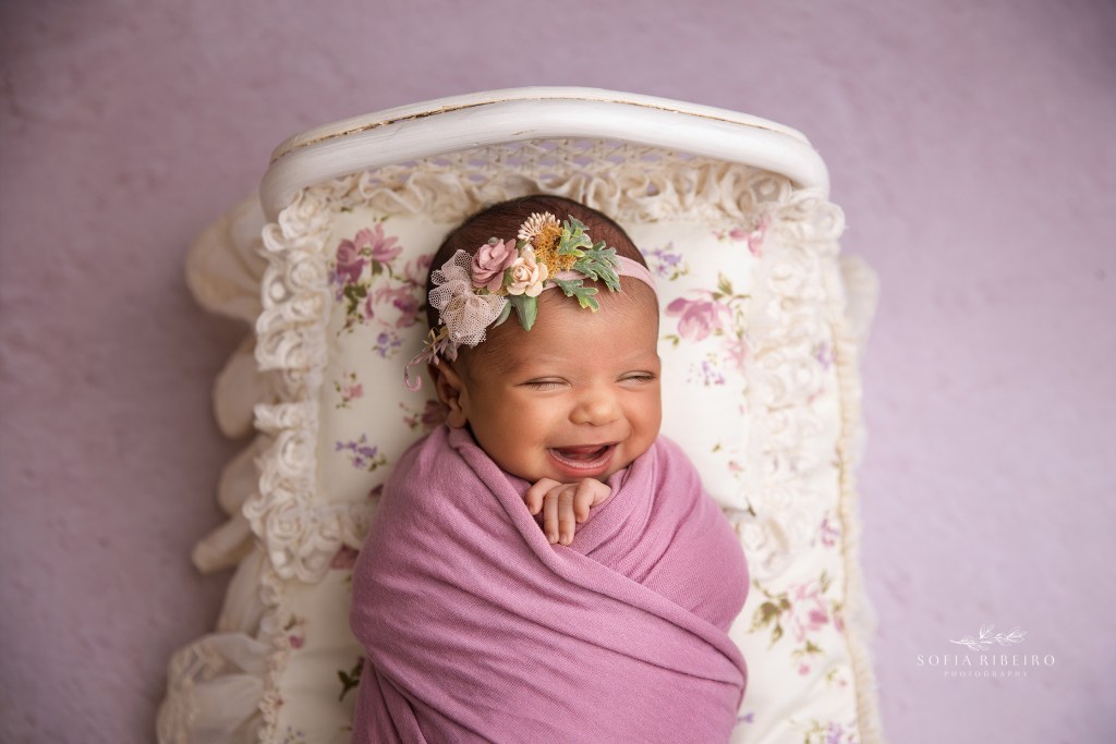 a big smile from baby girl wrapped in pink on a newborn bed prop
