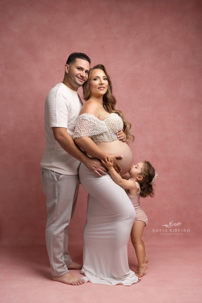 a family portrait with big sister kissing mom's baby bump during maternity portraits