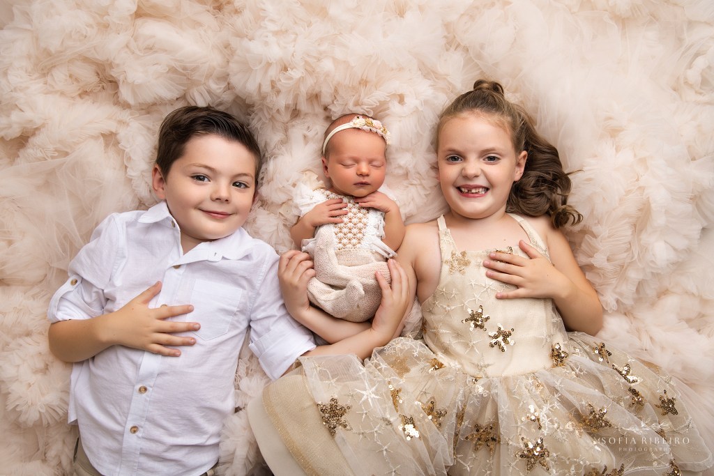 siblings smile to camera while cradling their baby sister