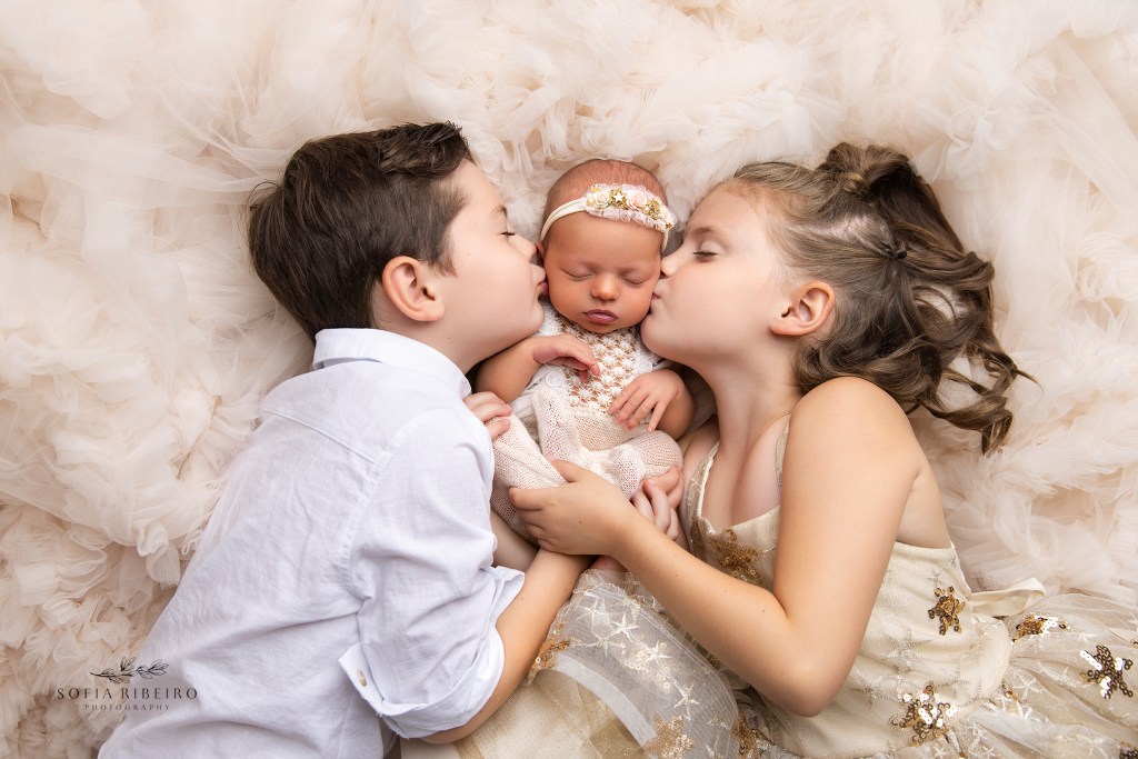siblings give their baby sister a kiss during newborn portraits