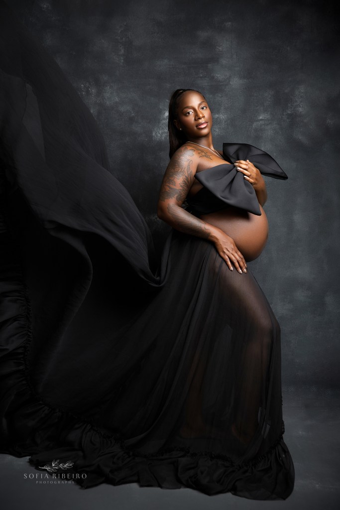 mom to be is elegant with a flowing black gown and bow top for maternity photos